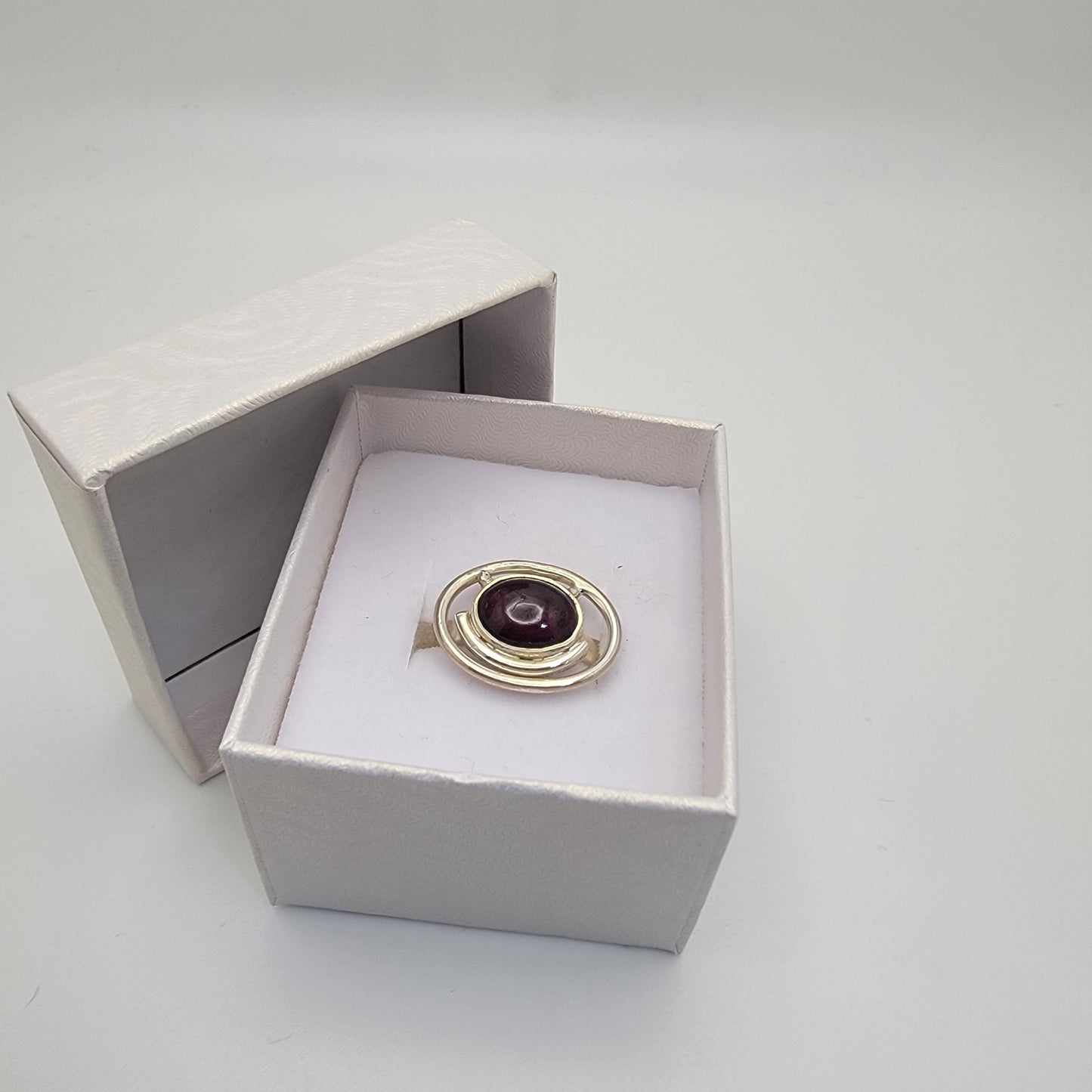 Sterling silver ring with a 12×10 mm oval garnet cabochon set on a uniform 3 mm band, displayed in a gift box.