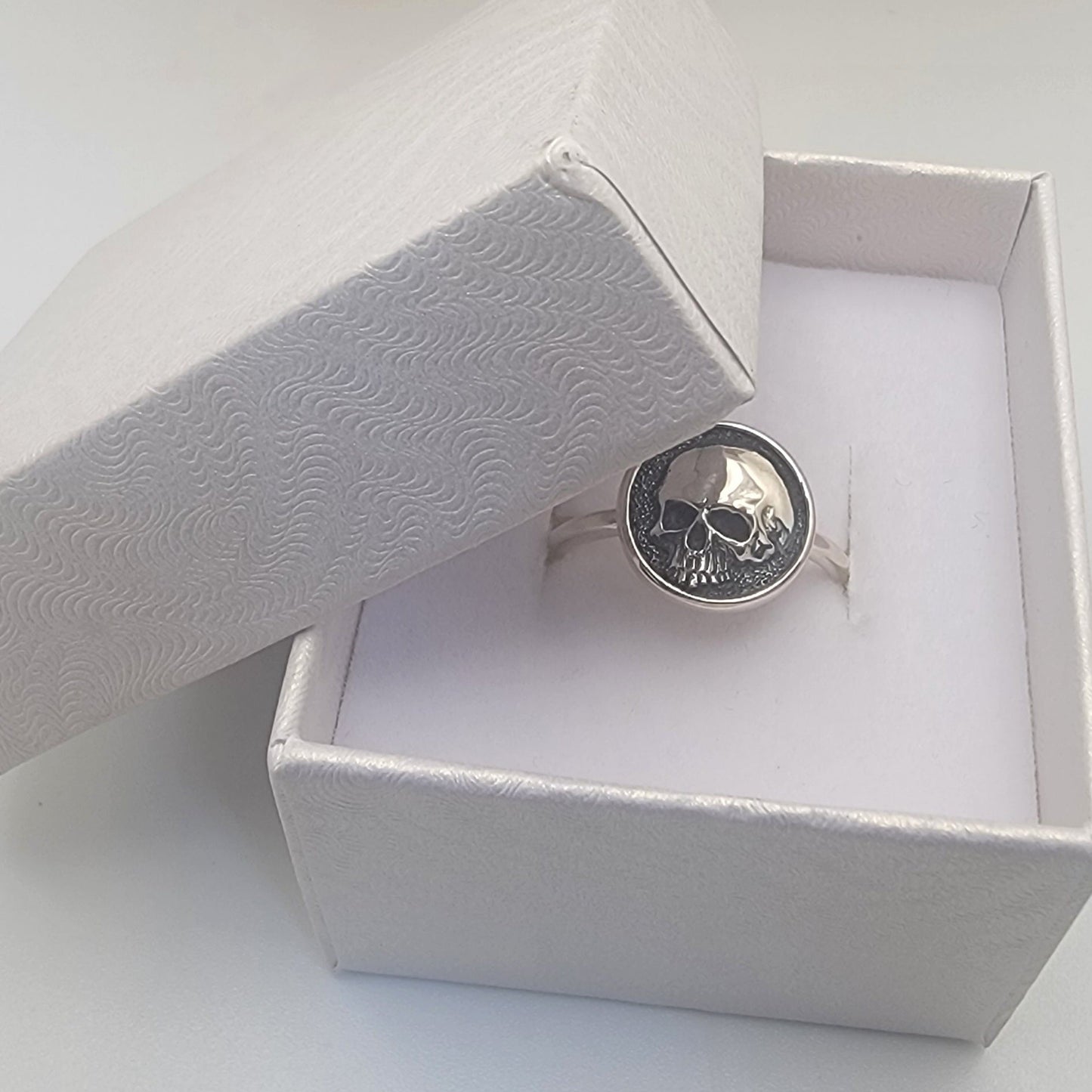Silver ring with a skull design in an open white jewelry box