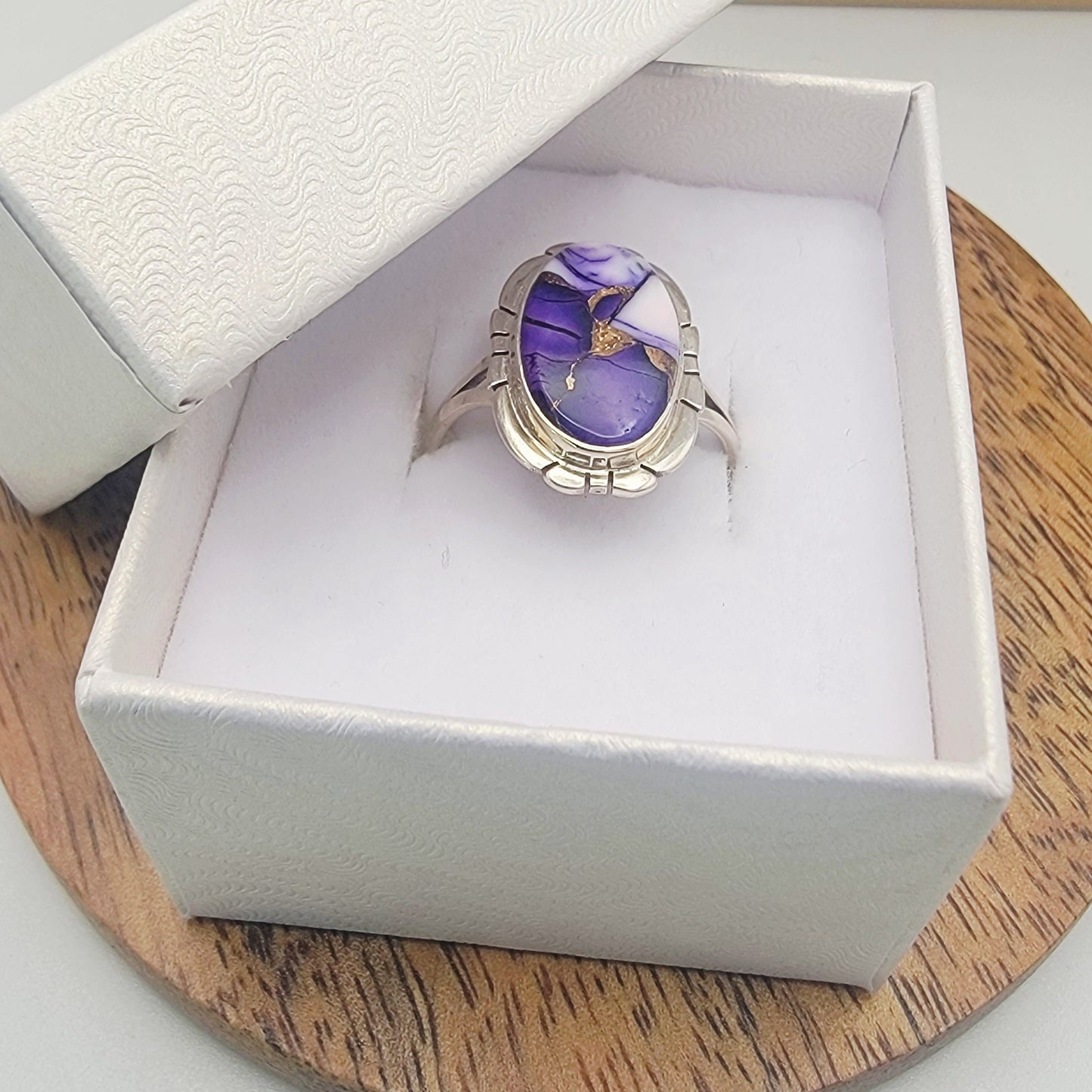 Silver ring with a purple stone in a white box on a wooden surface