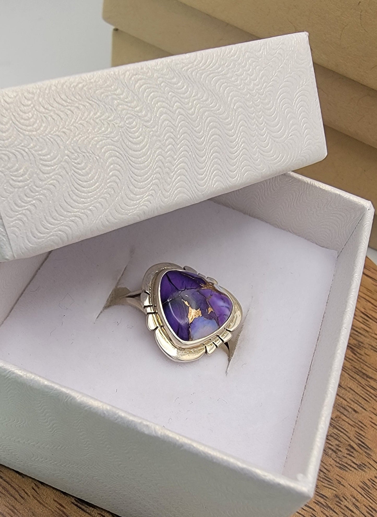 Silver ring with a purple stone in a white box on a wooden surface