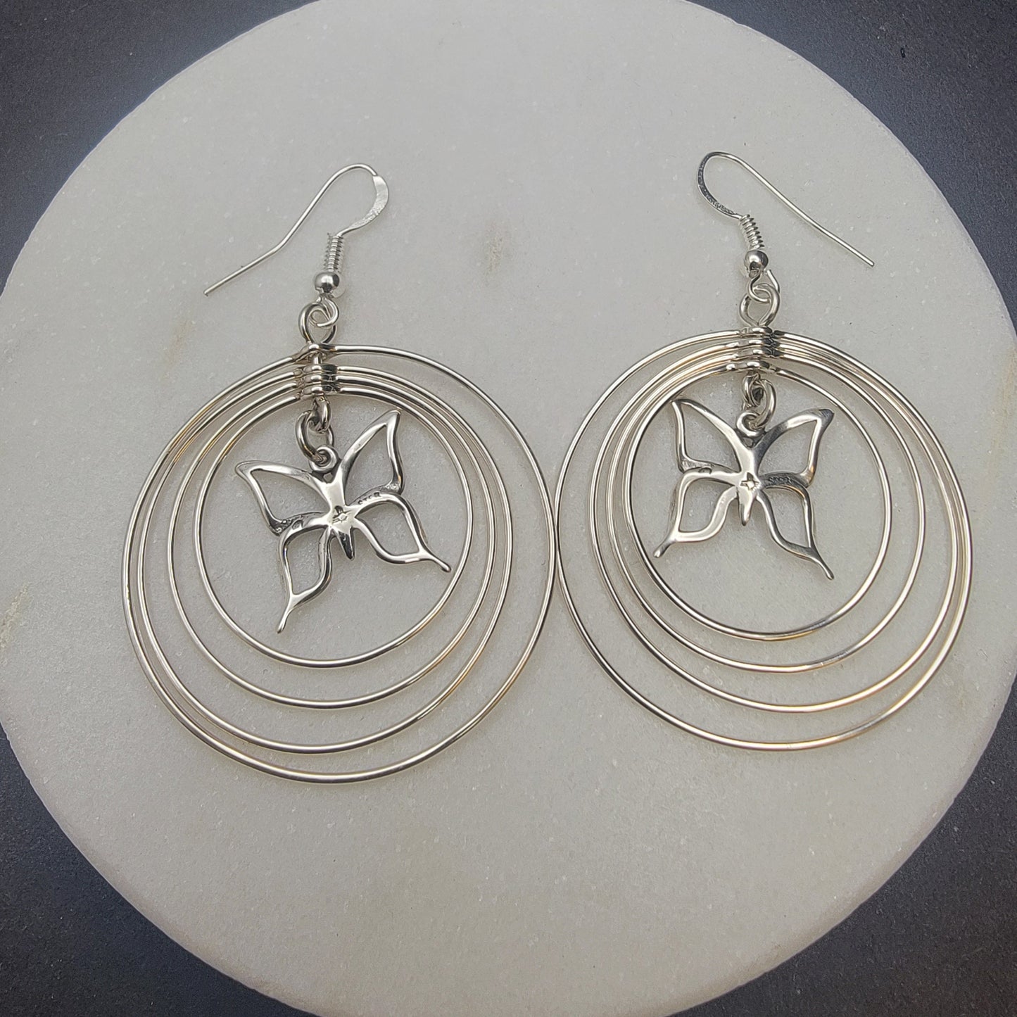 Sterling silver concentric hoop earrings (2¼″ × 1½″) featuring four graduated rings framing a delicate butterfly charm.
