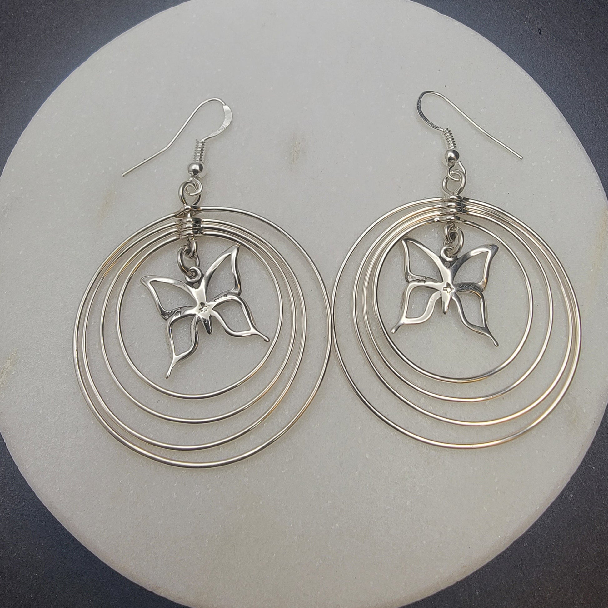 Sterling silver concentric hoop earrings (2¼″ × 1½″) featuring four graduated rings framing a delicate butterfly charm.