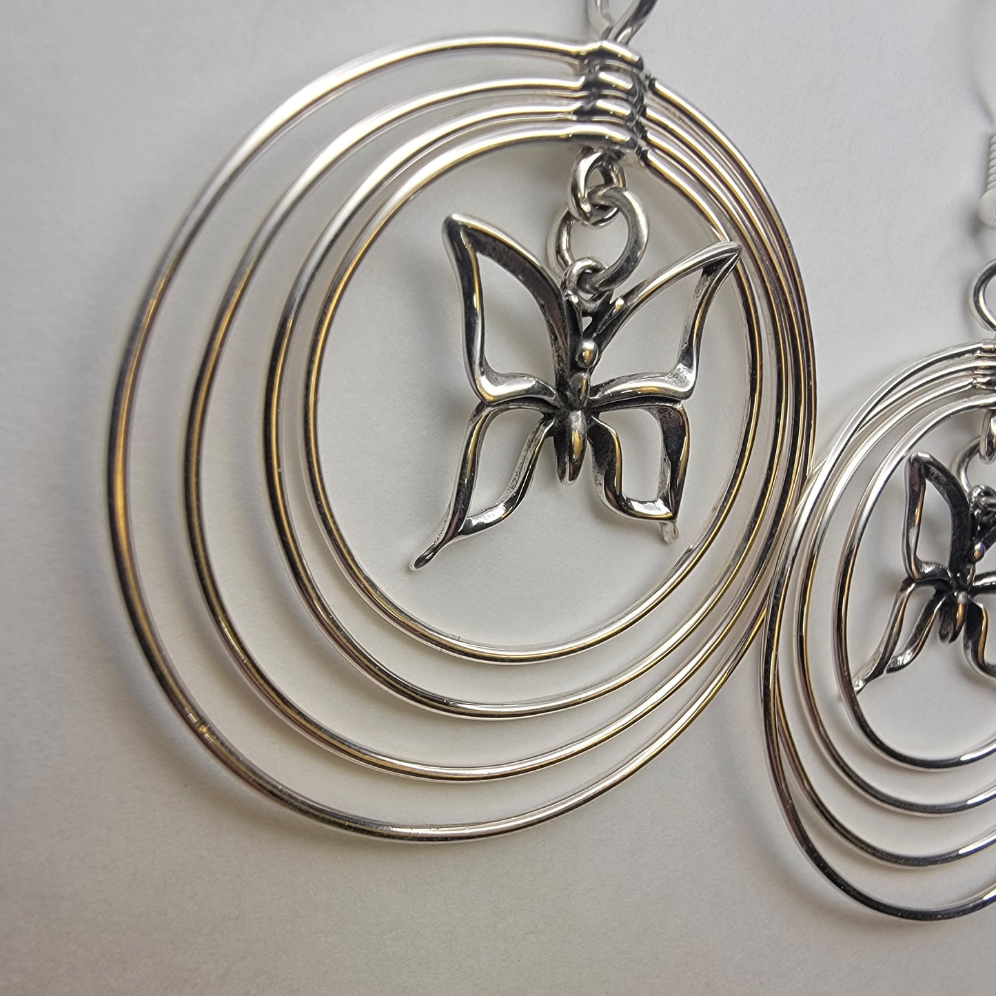 Sterling silver concentric hoop earrings (2¼″ × 1½″) featuring four graduated rings framing a delicate butterfly charm.