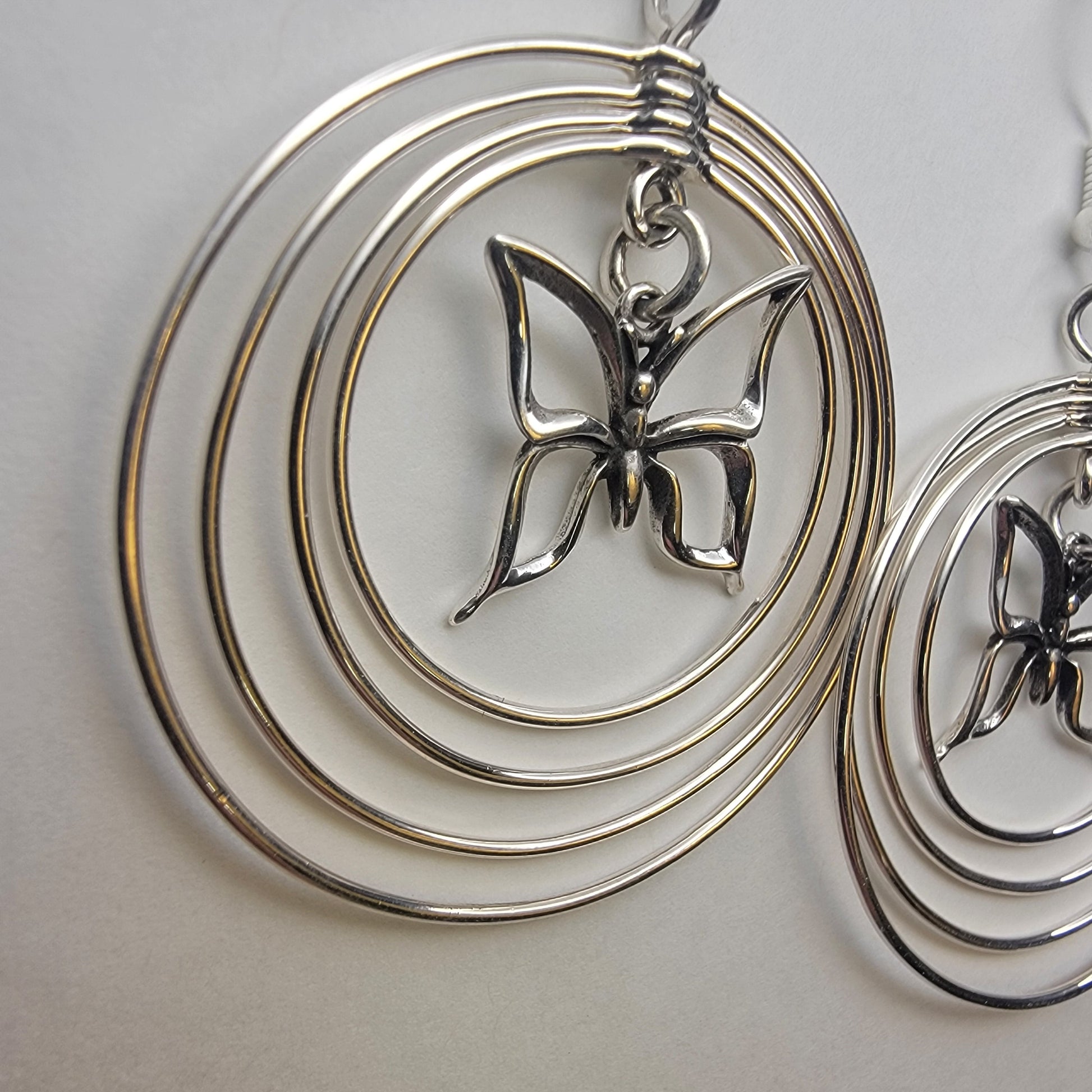 Sterling silver concentric hoop earrings (2¼″ × 1½″) featuring four graduated rings framing a delicate butterfly charm.