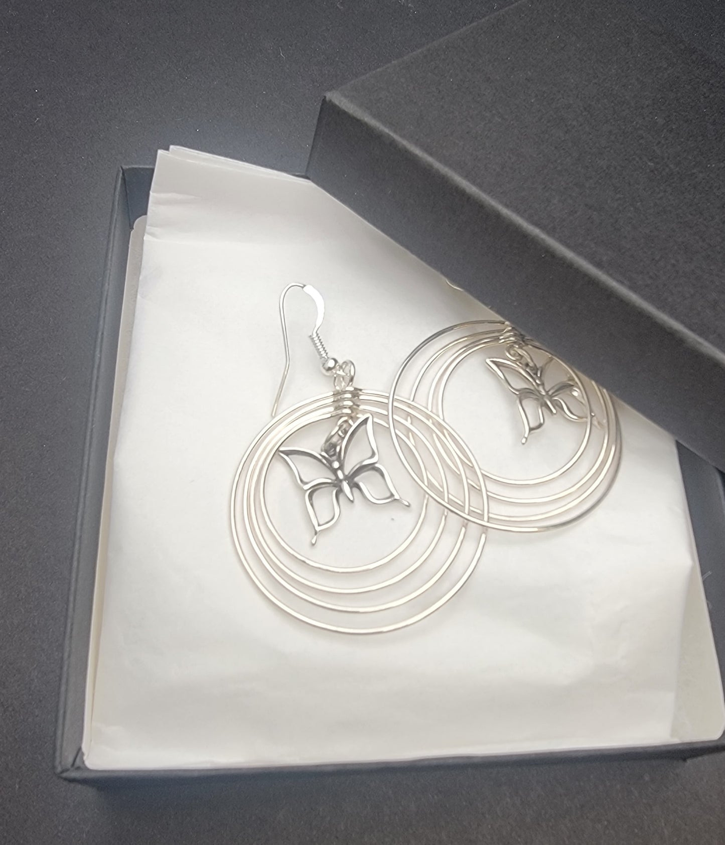 Sterling silver concentric hoop earrings (2¼″ × 1½″) featuring four graduated rings framing a delicate butterfly charm.