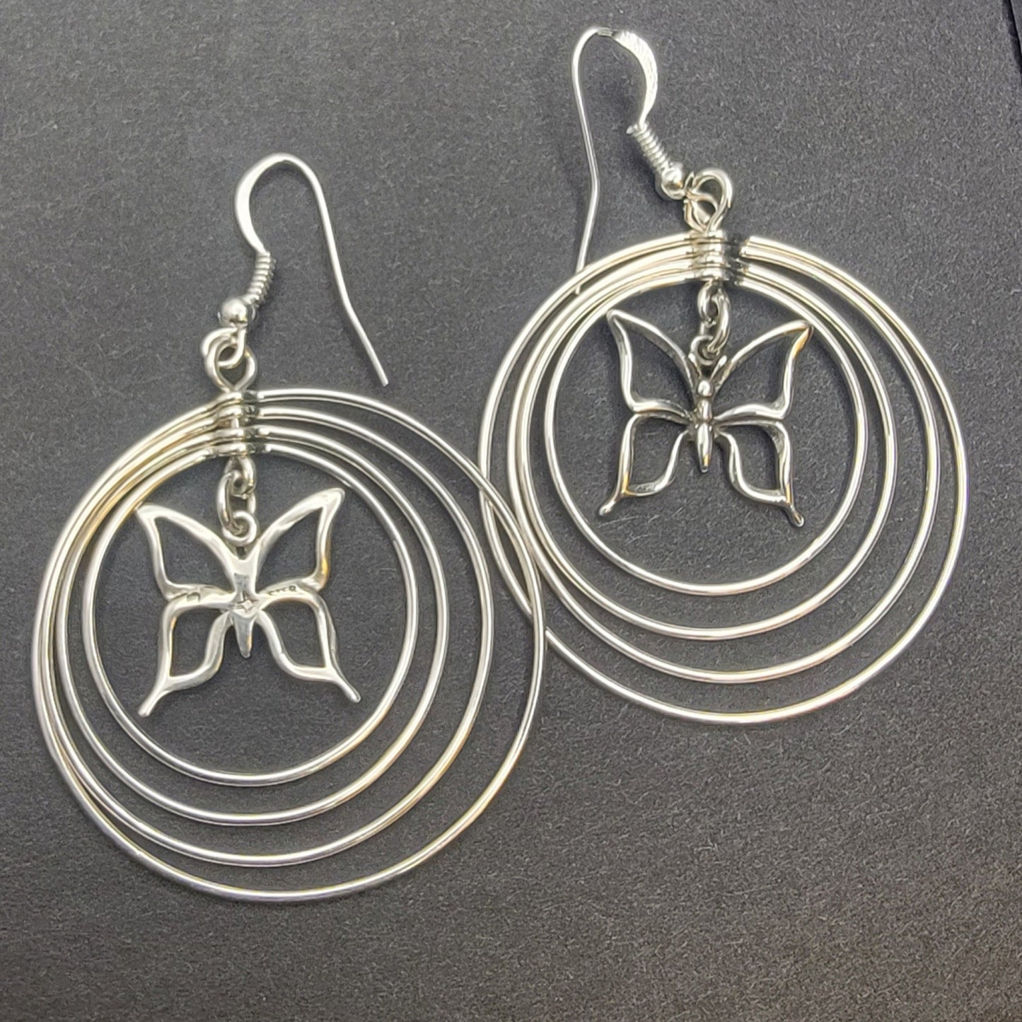 Sterling silver concentric hoop earrings (2¼″ × 1½″) featuring four graduated rings framing a delicate butterfly charm.