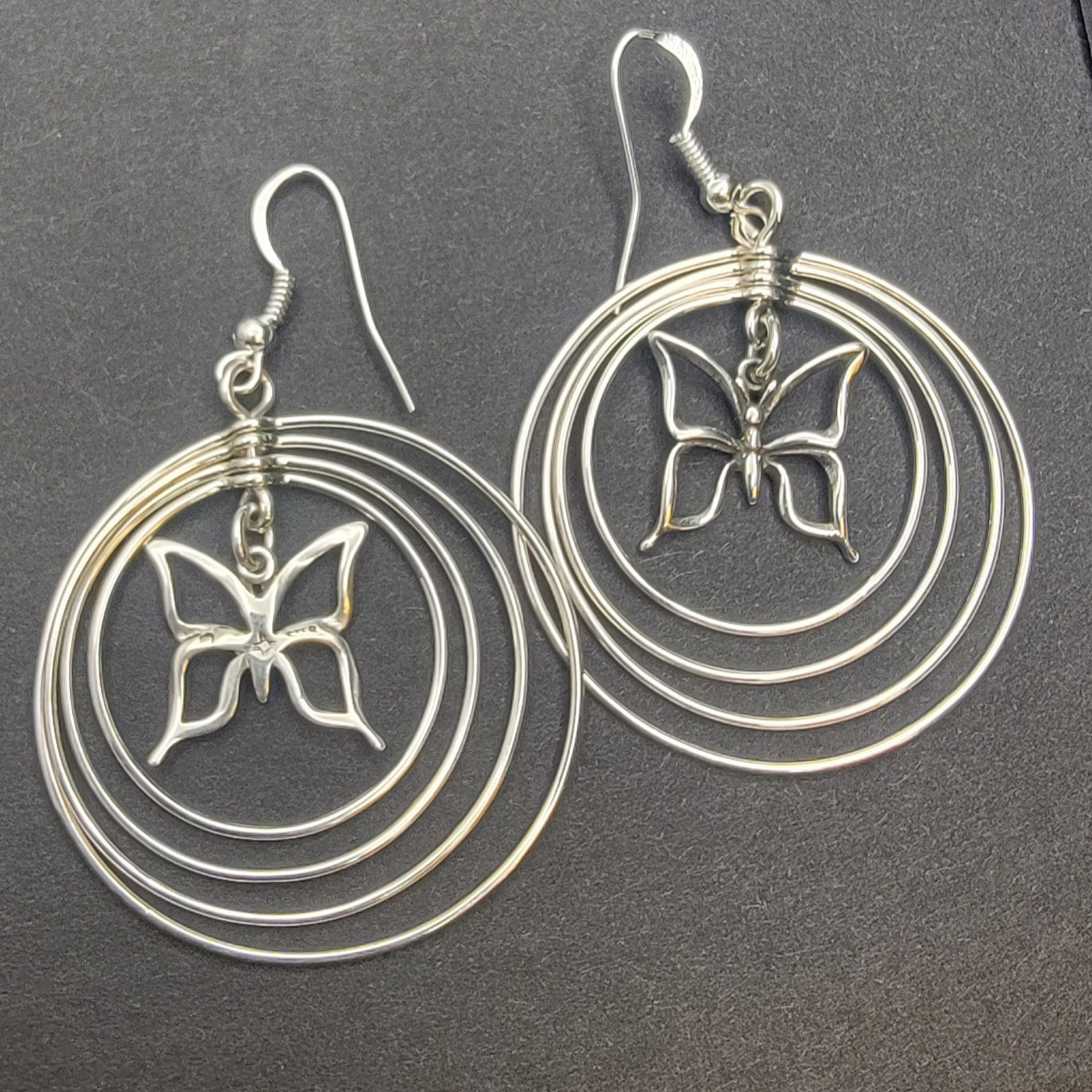 Sterling silver concentric hoop earrings (2¼″ × 1½″) featuring four graduated rings framing a delicate butterfly charm.