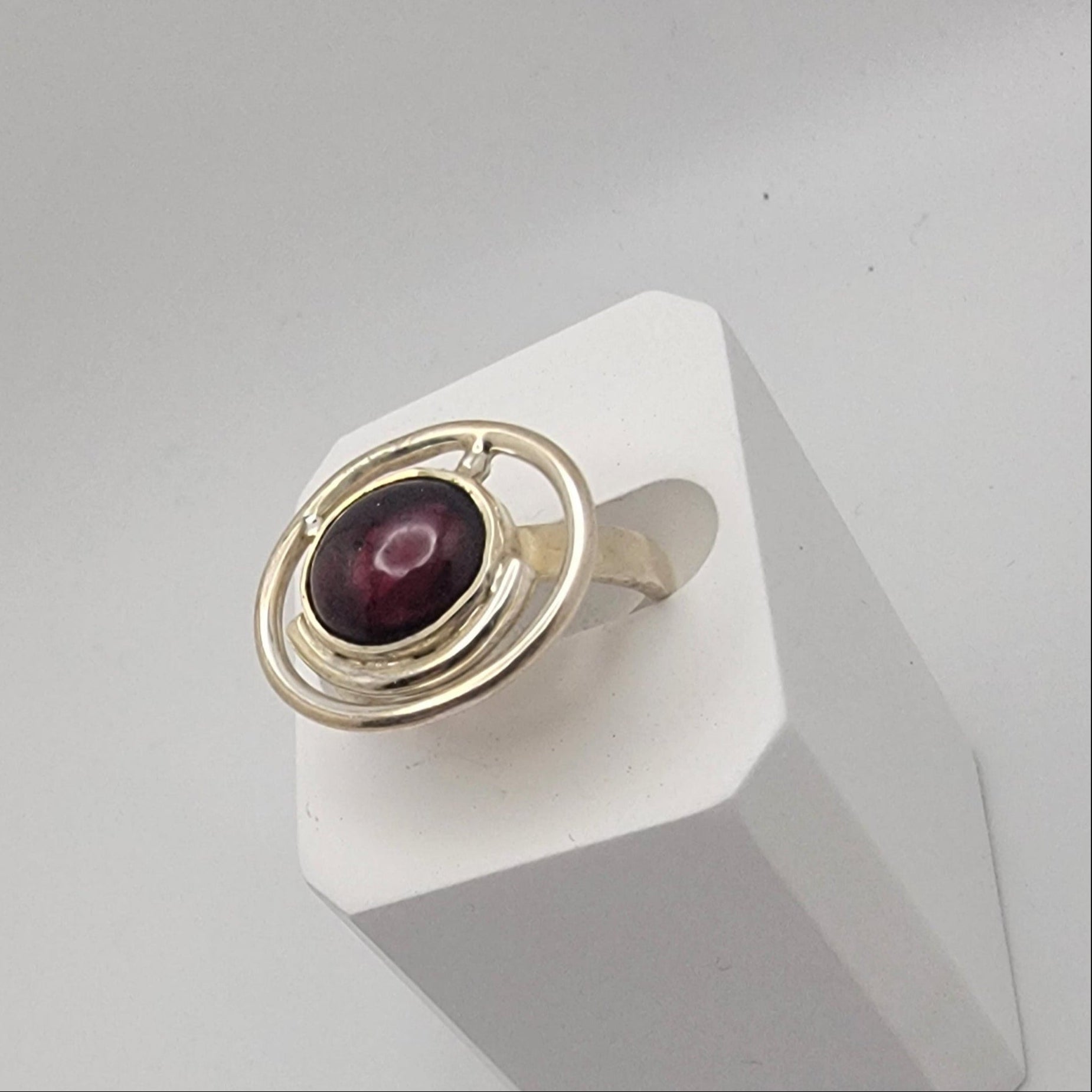 Sterling silver ring with a 12×10 mm oval garnet cabochon set on a uniform 3 mm band, displayed on a white stand.