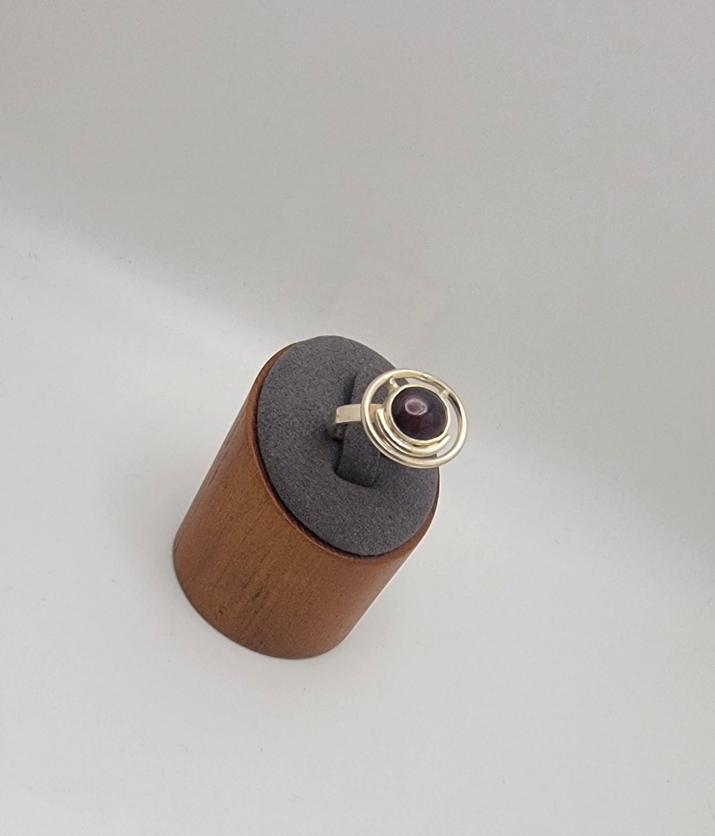 Sterling silver ring with a 12×10 mm oval garnet cabochon set on a uniform 3 mm band, displayed on a wooden stand.