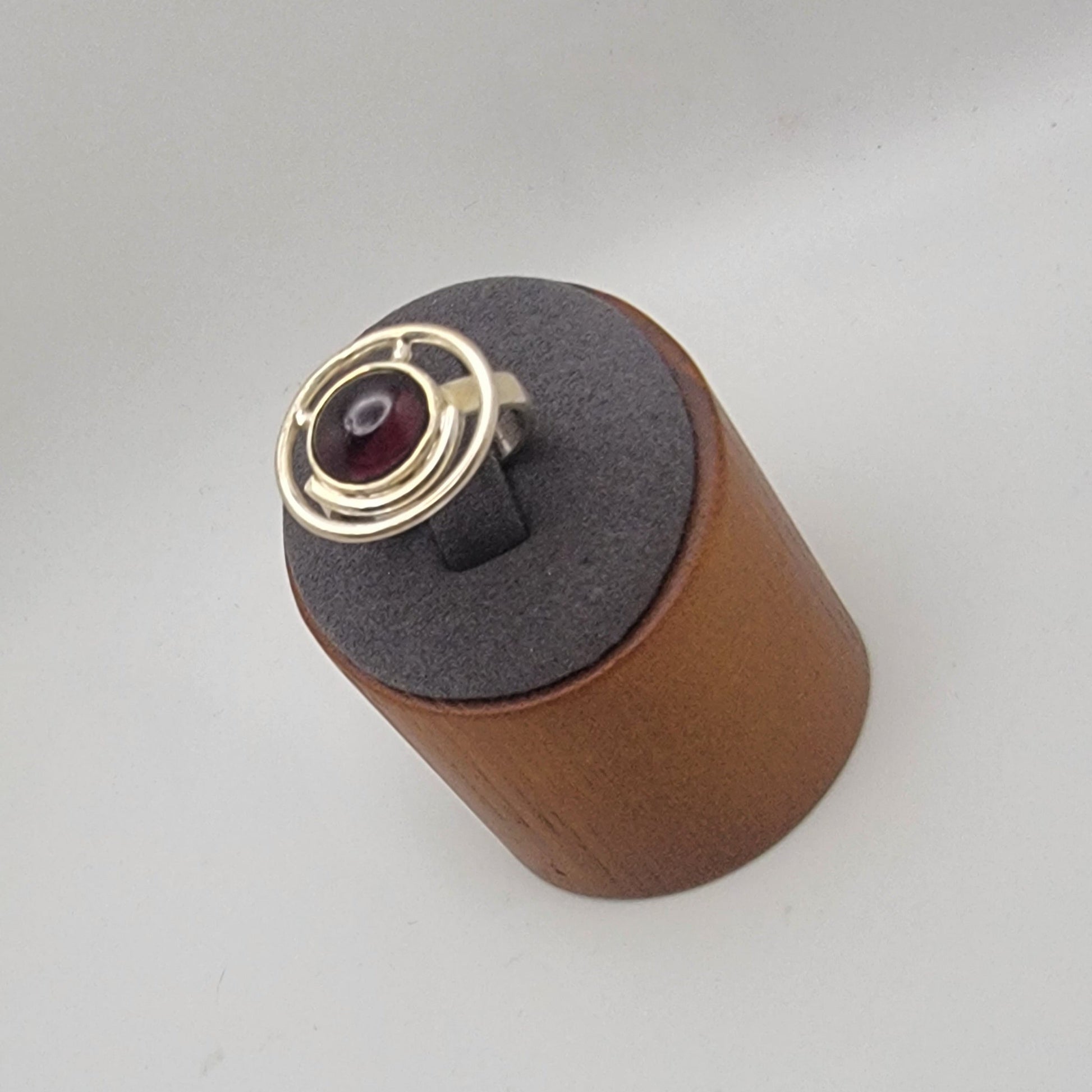 Sterling silver ring with a 12×10 mm oval garnet cabochon set on a uniform 3 mm band, displayed on a wooden stand.