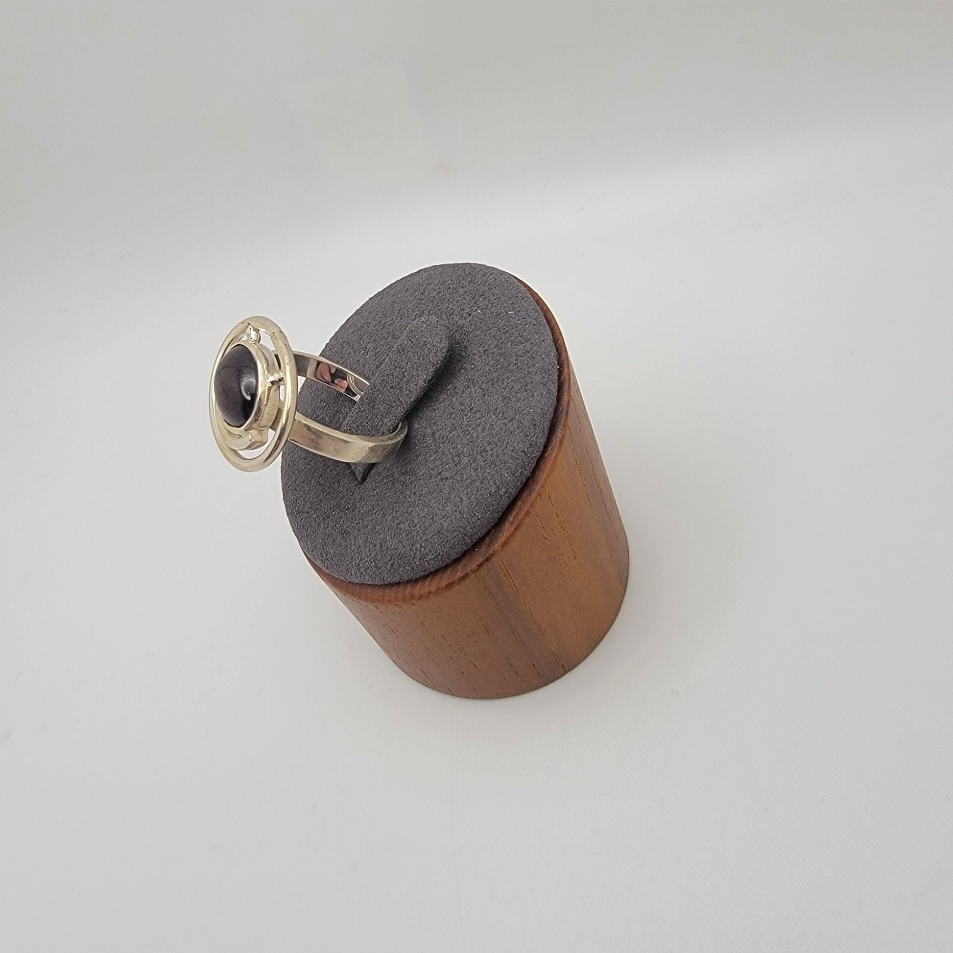 Sterling silver ring with a 12×10 mm oval garnet cabochon set on a uniform 3 mm band, displayed on a wooden stand.