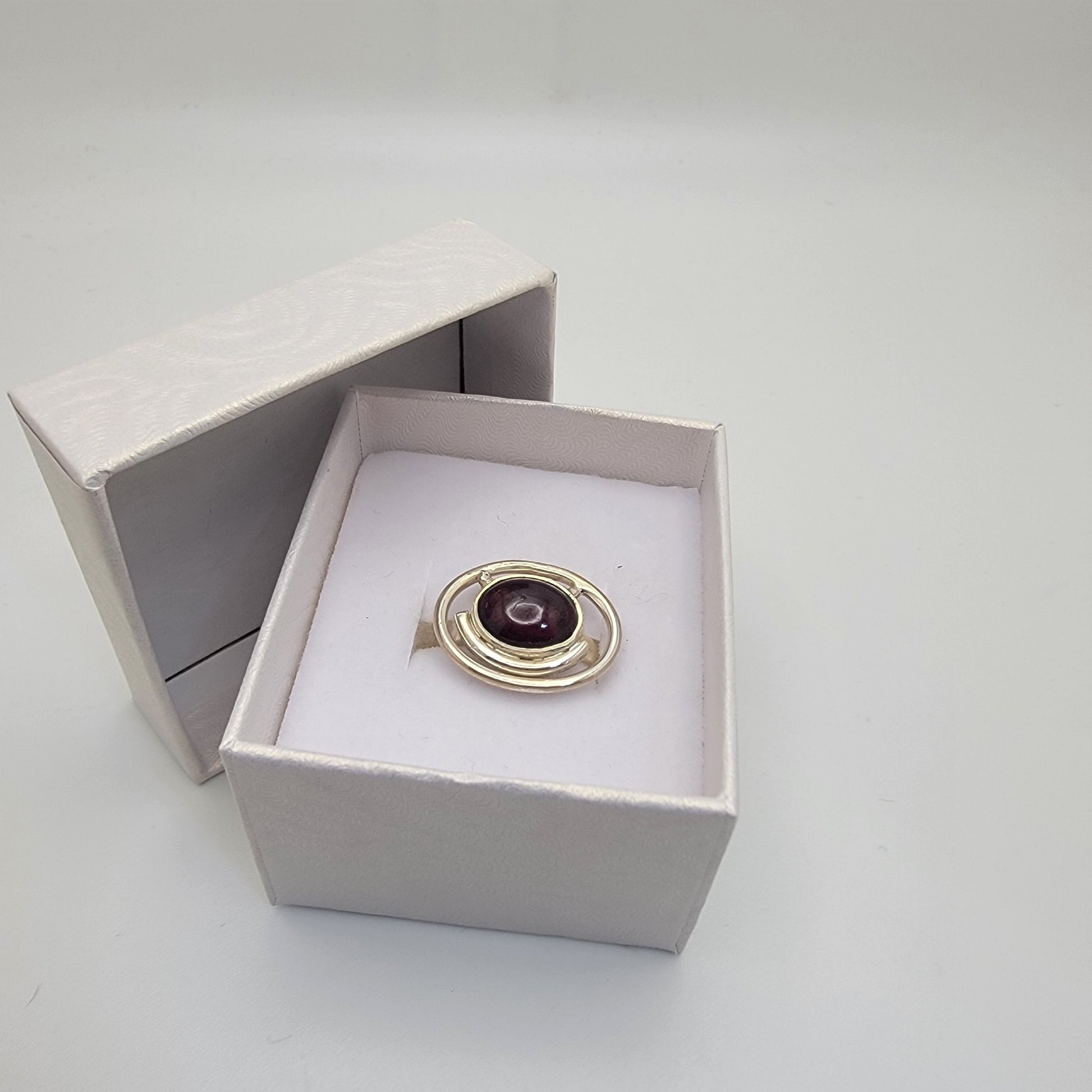 Sterling silver ring with a 12×10 mm oval garnet cabochon set on a uniform 3 mm band, displayed in a gift box.