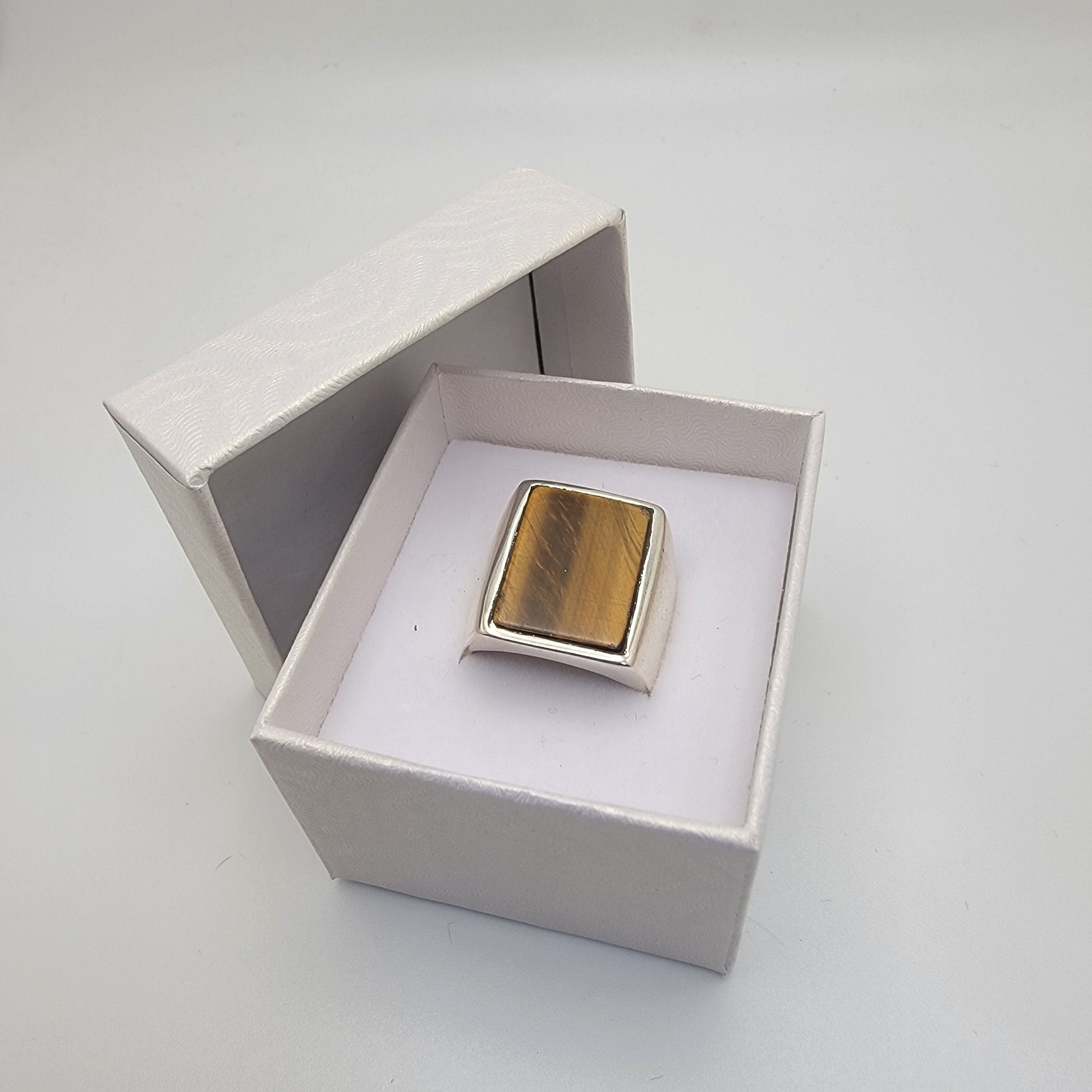 Silver ring with rectangular tiger's eye cabochon in grey and wooden stand