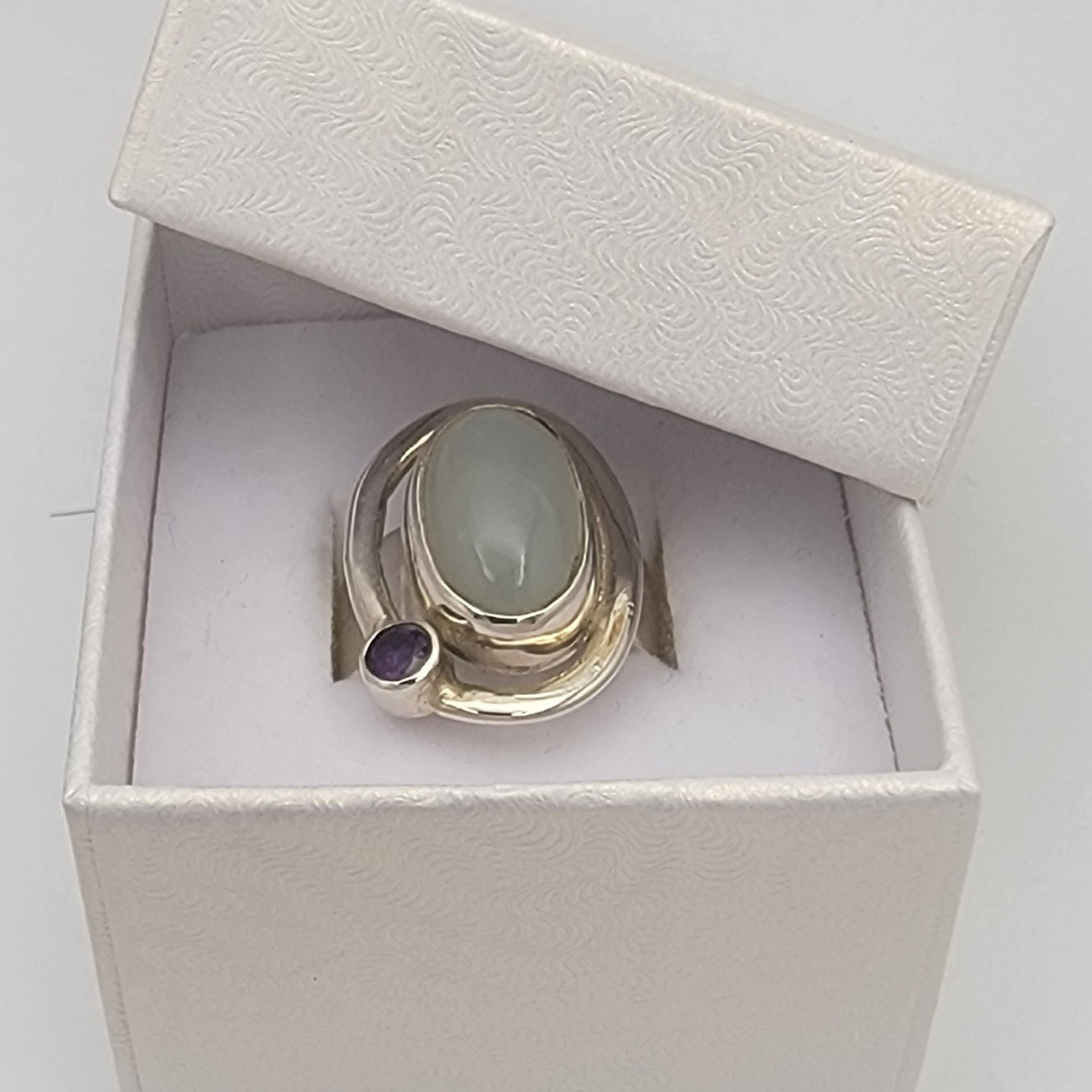 Silver ring with a green stone and purple gemstone in a white box