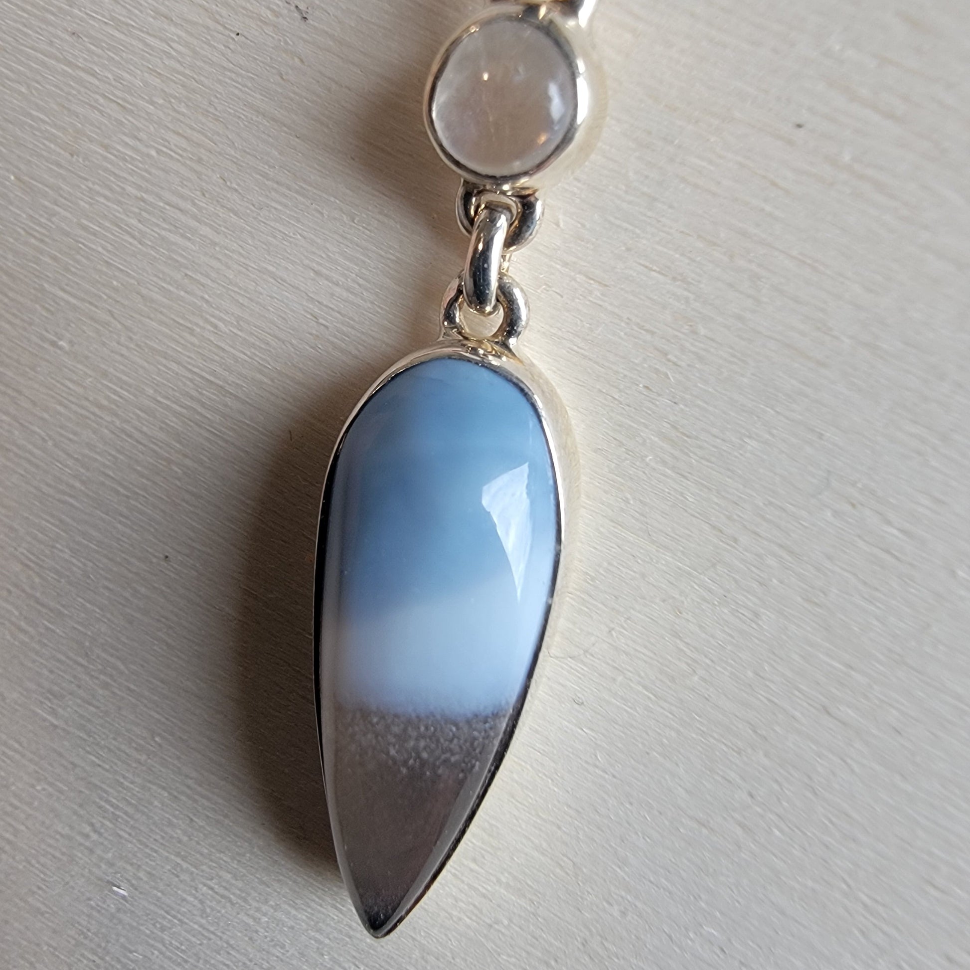 Jewelry with a blue teardrop pendant and silver chain on a light gray background