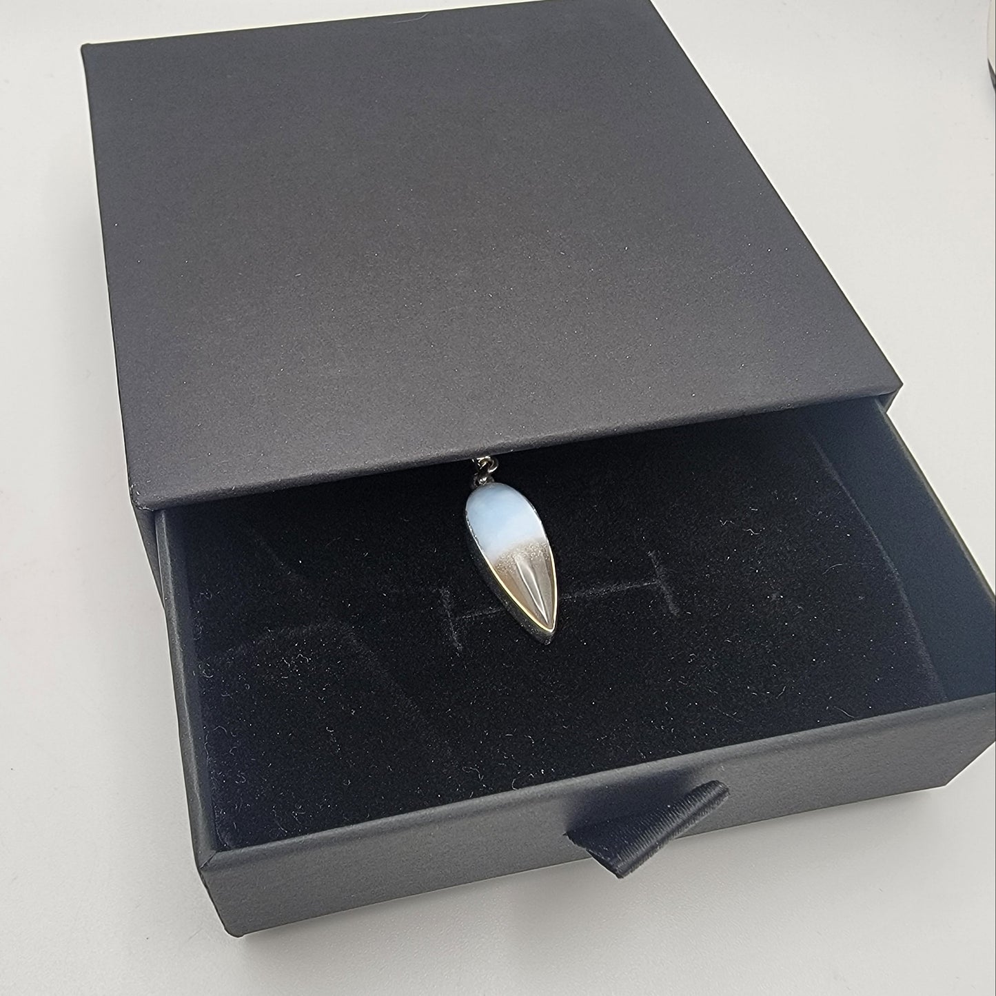 Open black jewelry box with a ring featuring a blue stone and silver band on a white background