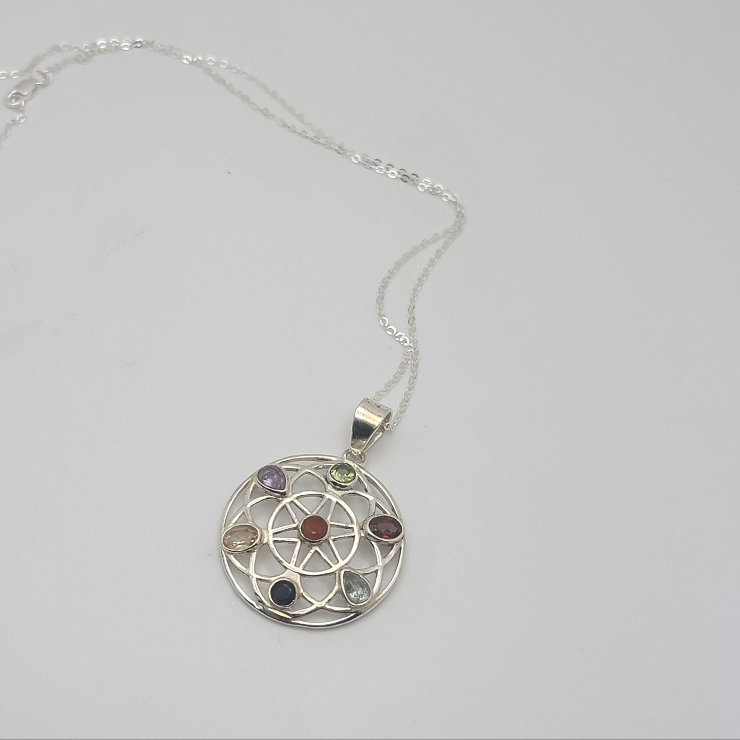 Silver necklace with a circular pendant featuring colorful stones on a light gray background
