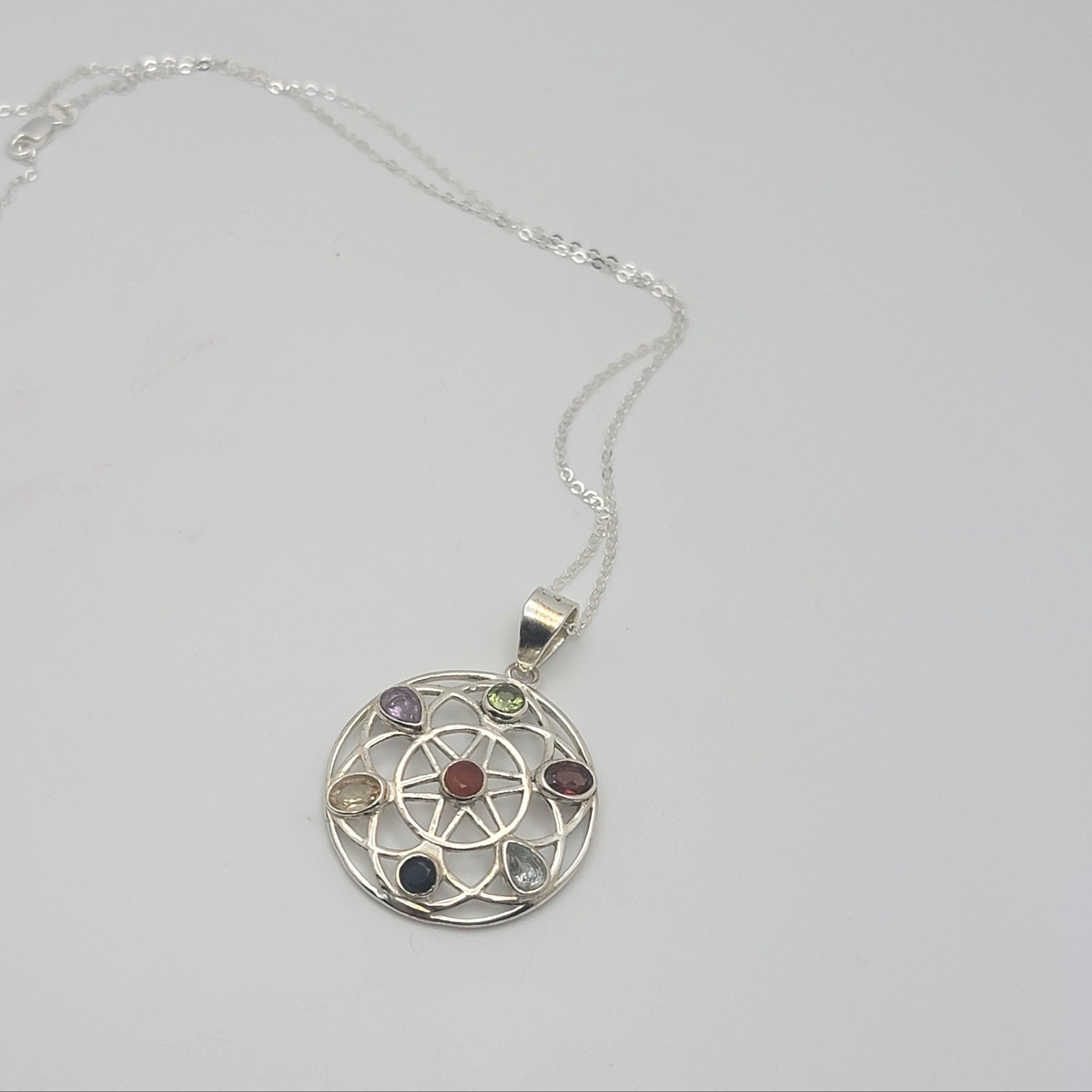 Silver necklace with a circular pendant featuring colorful stones on a light gray background