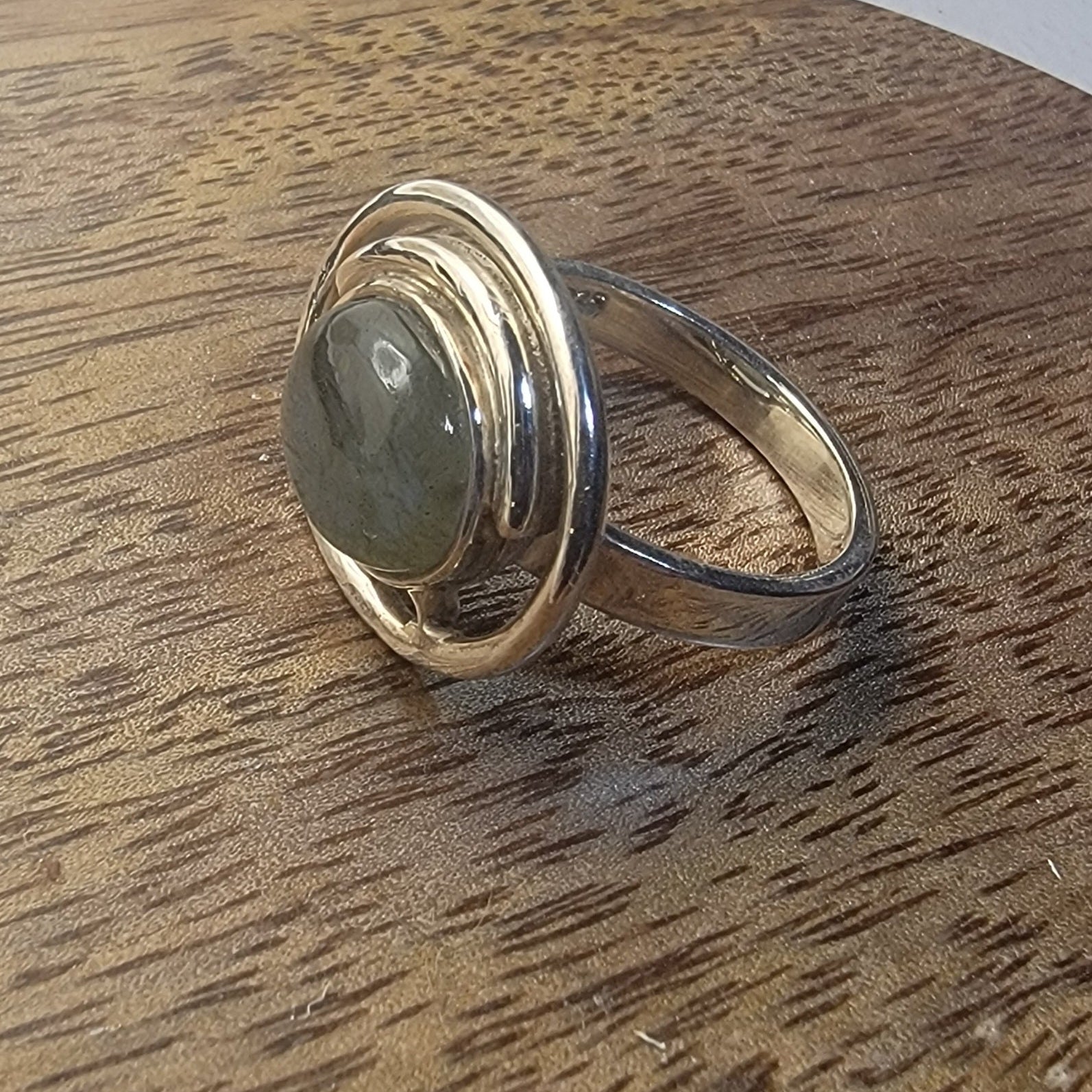 Silver ring with a labradorite stone on a wooden surface