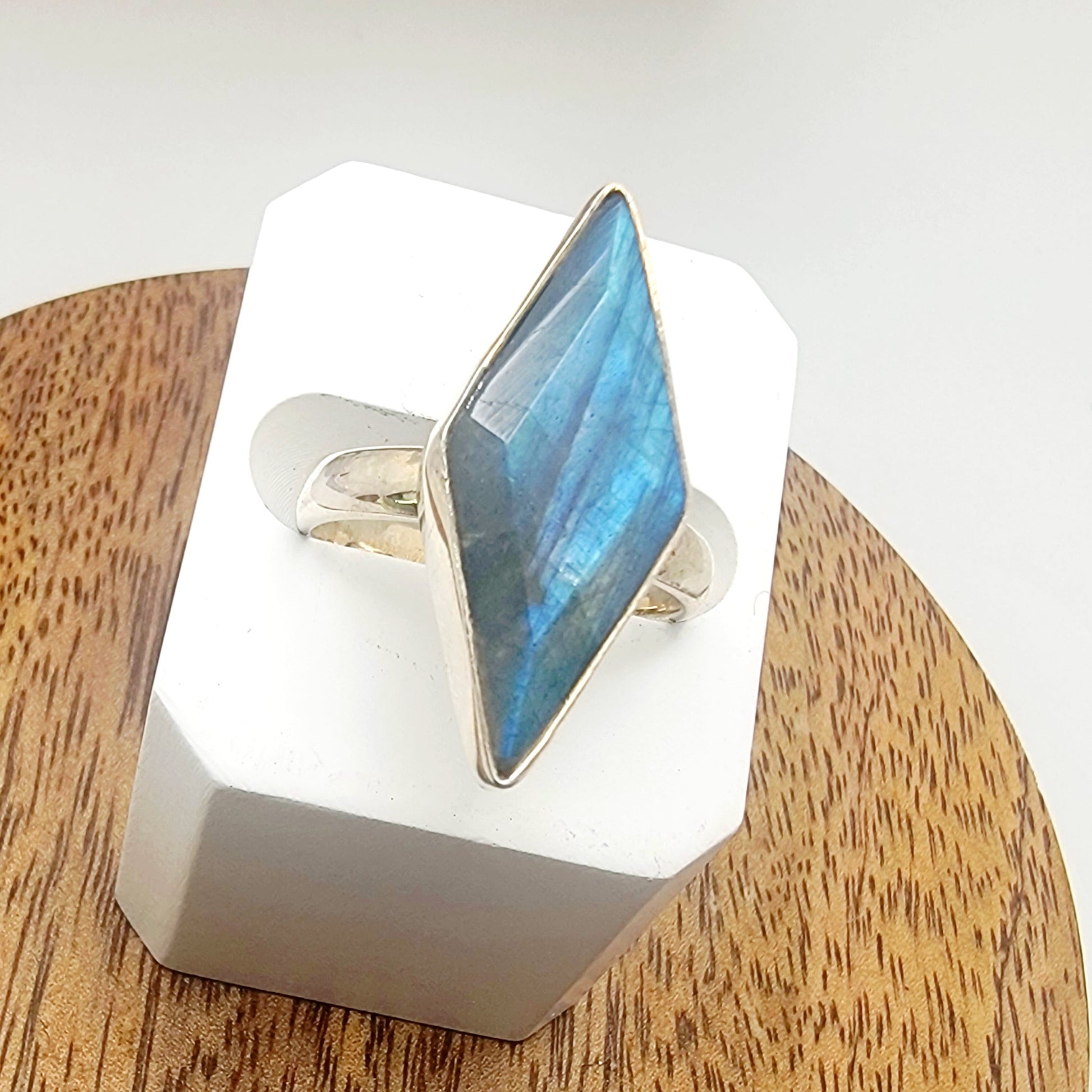 Silver ring with a labradorite stone on a white stand against a wooden surface