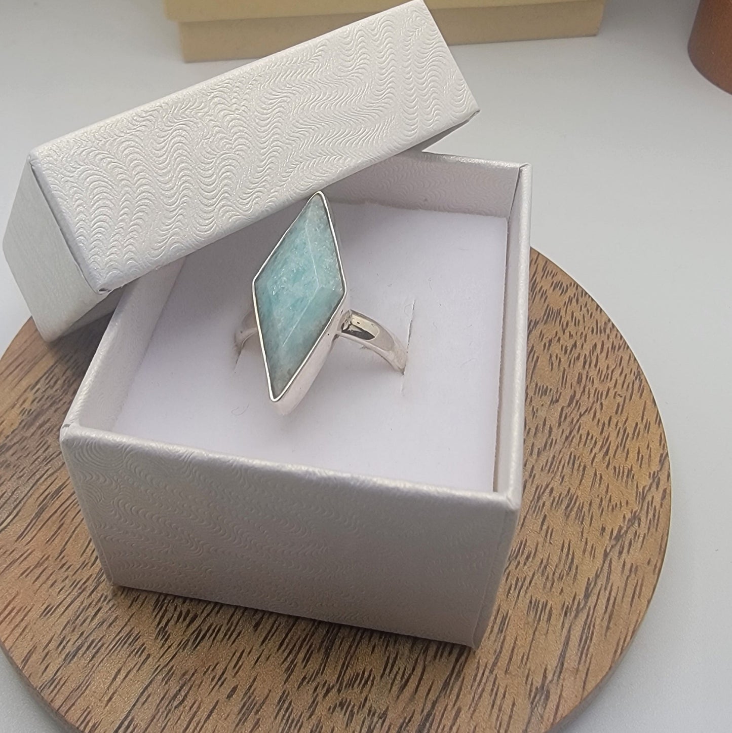 Silver ring with a blue larimar gemstone in an open jewelry box on a wooden surface.