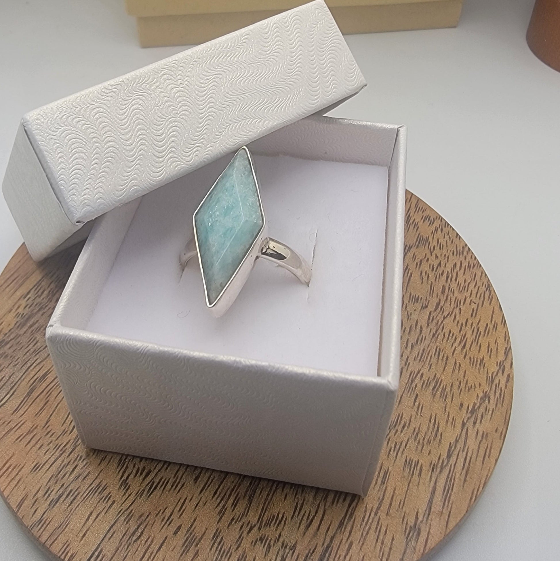 Silver ring with a blue larimar gemstone in an open jewelry box on a wooden surface.