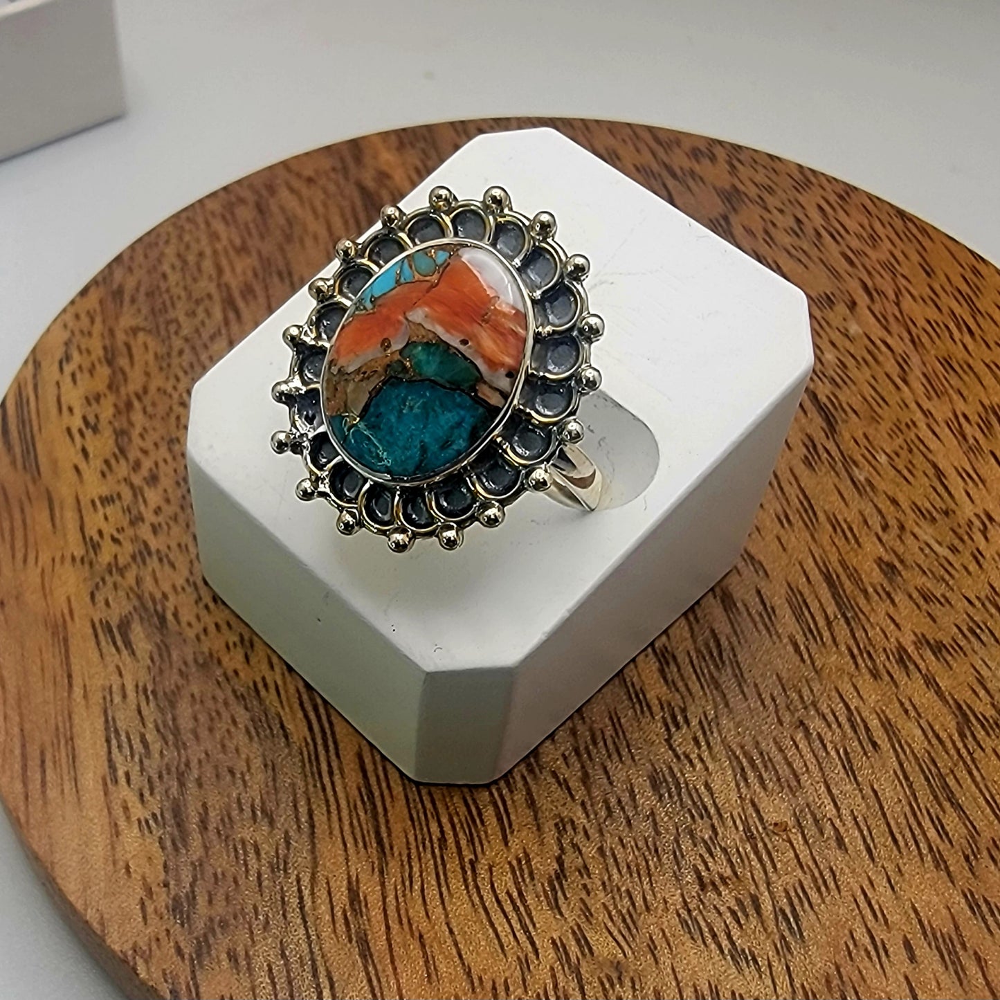 Sterling silver ring with colorful stone on a white stand on a wooden surface