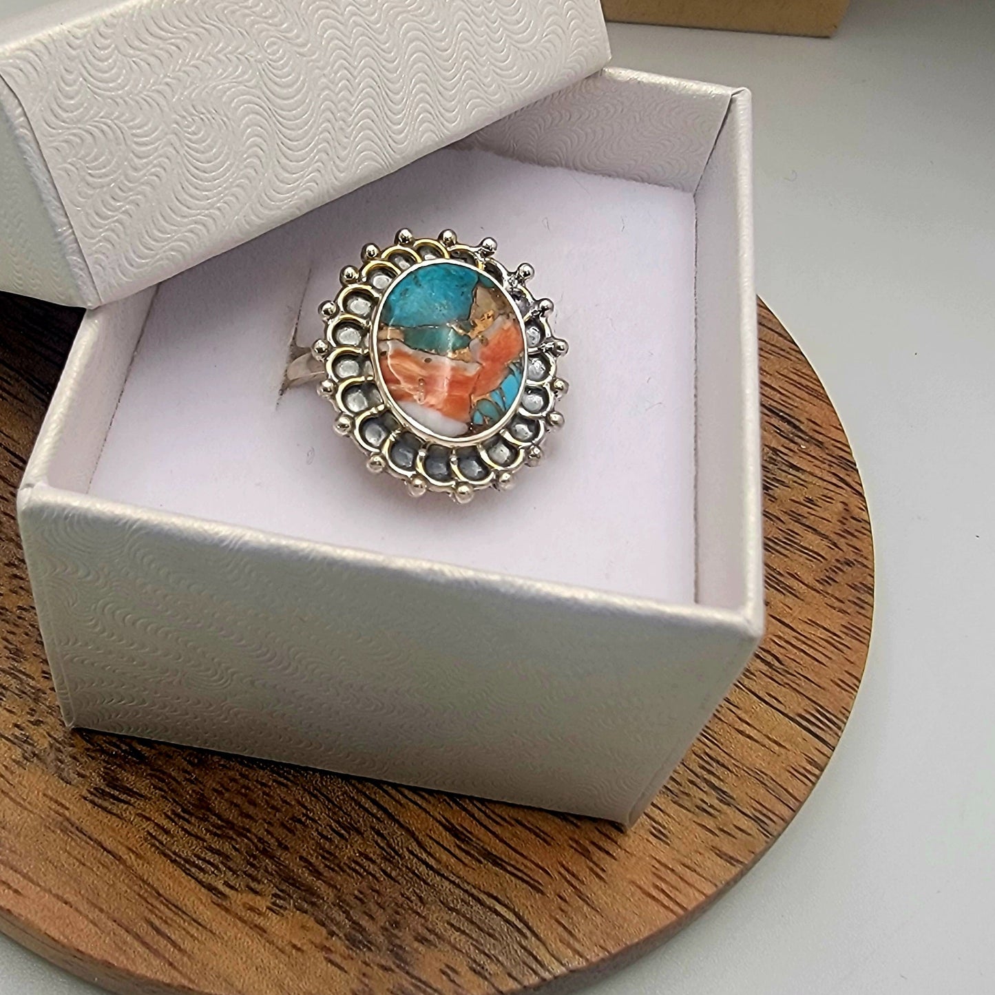 Silver ring with colorful stone in a white box on a wooden surface
