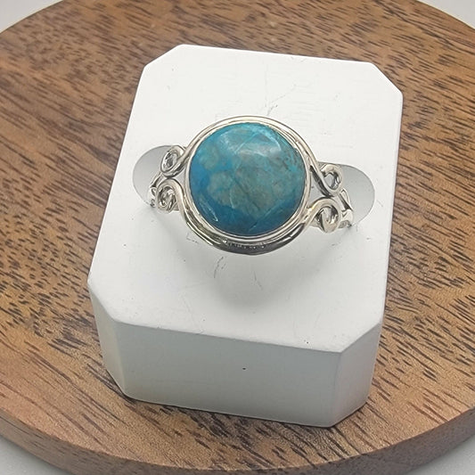 Silver ring with a blue stone on a white stand against a wooden background