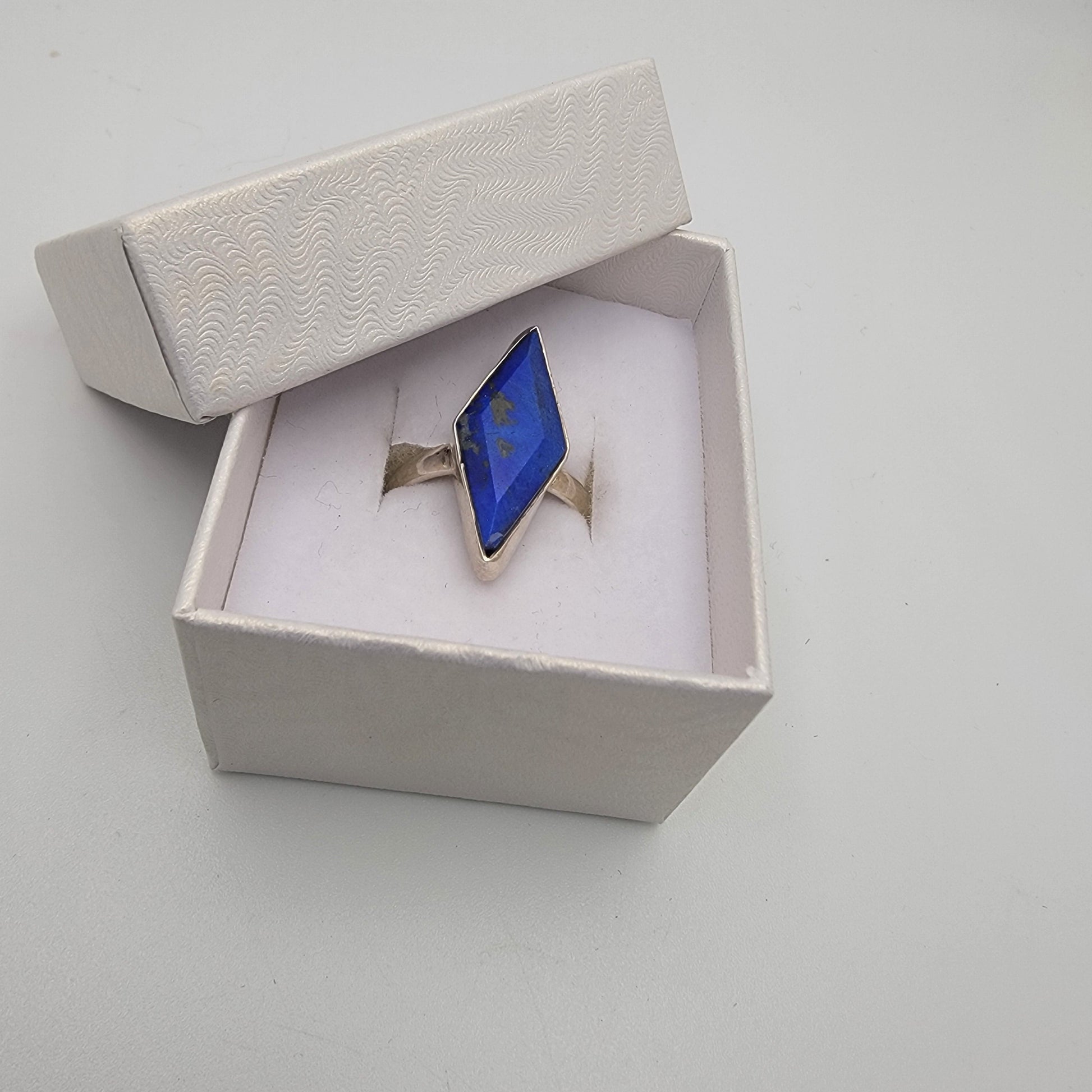 Sterling silver ring with blue lapis gemstone and gold accents in an open box on a light gray background
