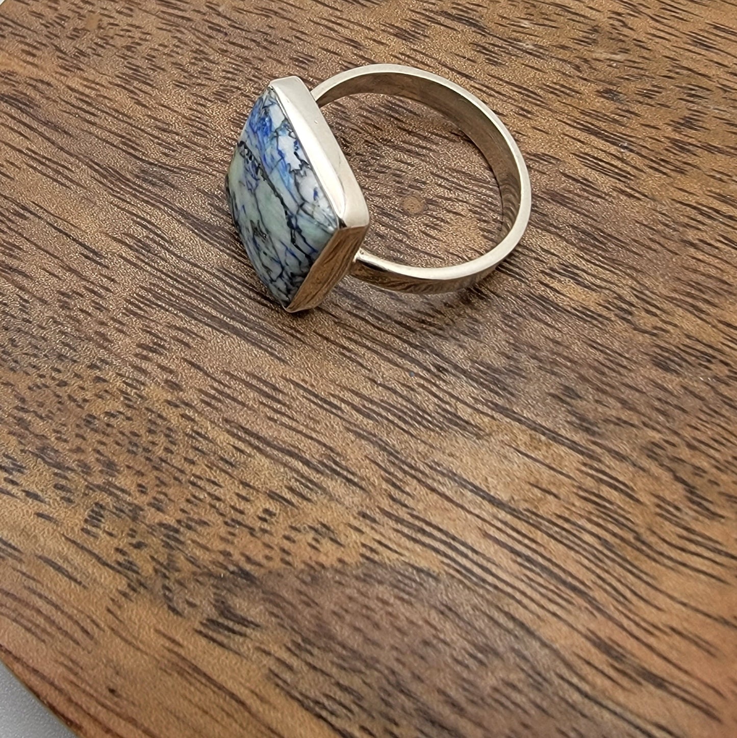 Silver ring with a blue and white patterned stone on a wooden surface