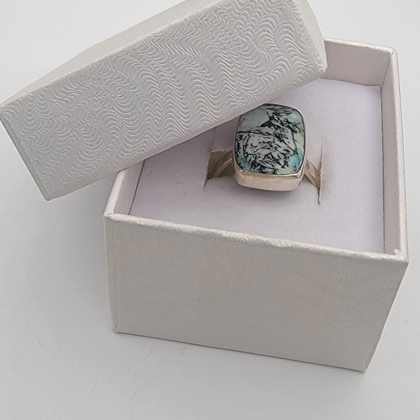 Jewelry box with a ring featuring a green gemstone on a light gray background