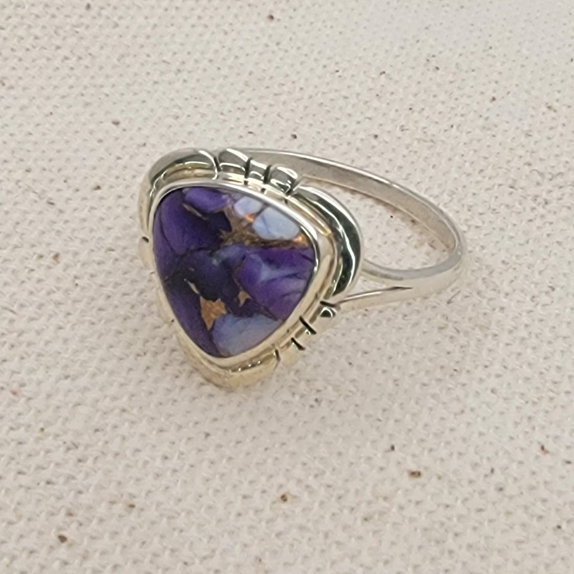 Silver ring with a purple triangular stone on a beige fabric background