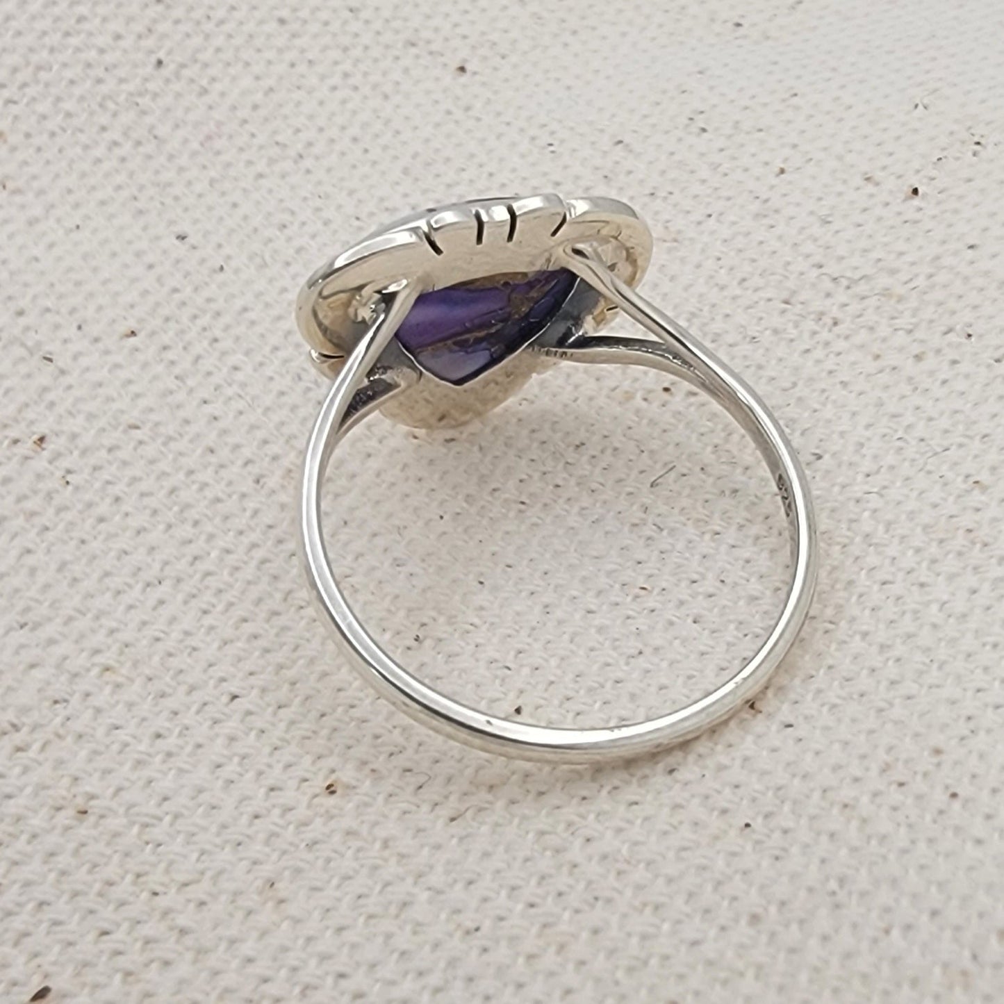 Silver ring with a purple gemstone on a textured beige surface
