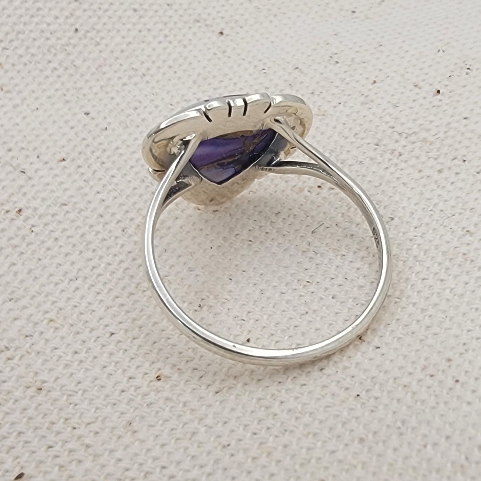 Silver ring with a purple gemstone on a textured beige surface