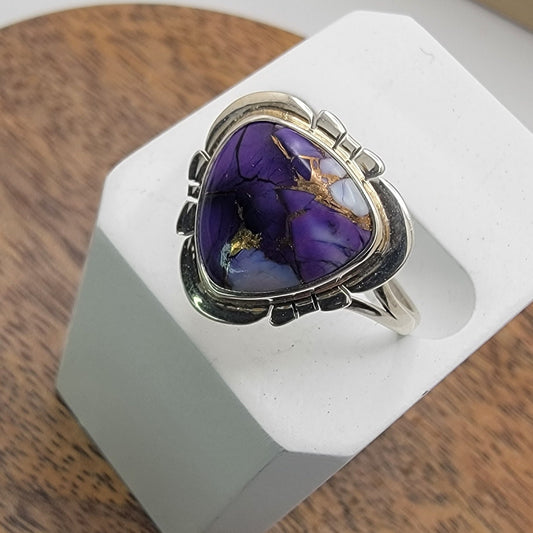 Silver ring with a purple stone on a white stand against a wooden background