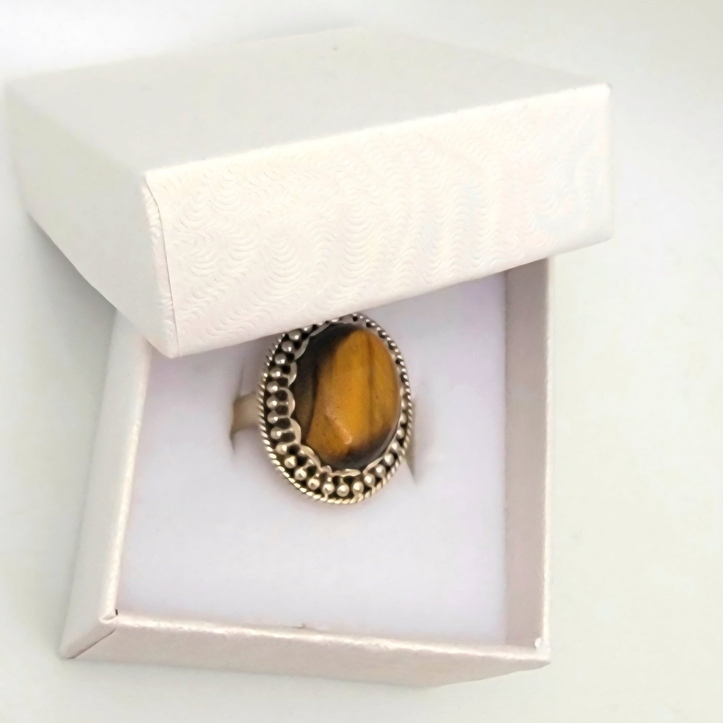 Ring with a tiger's eye stone in a white box on a light gray background